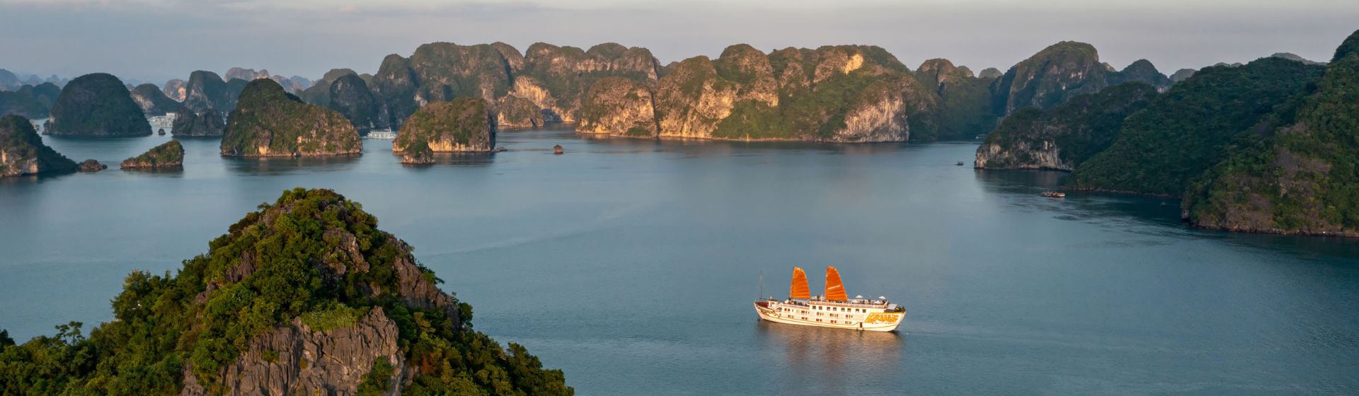 Aerial view of Indochina Sails Cruise ship sailing amongst limestone karsts in Ha Long Bay, Vietnam