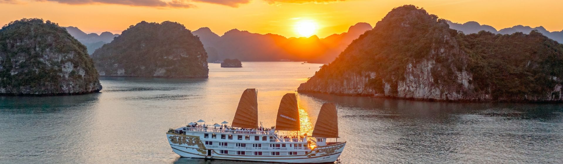 Indochina Sails Cruise Ship sailing past dramatic karsts during sunset at Ha Long Bay in Vietnam