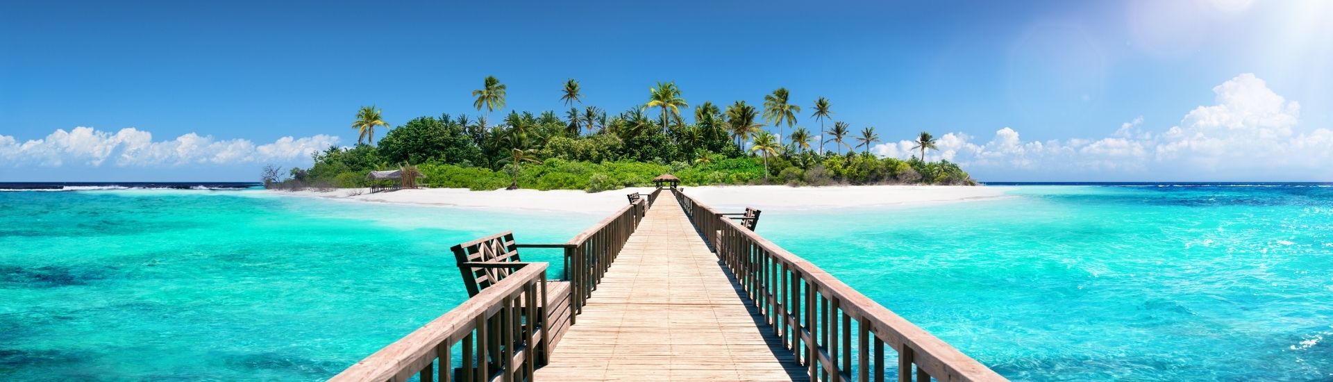 View from a jetty looking back to a tropical island with lush greenery, Maldives