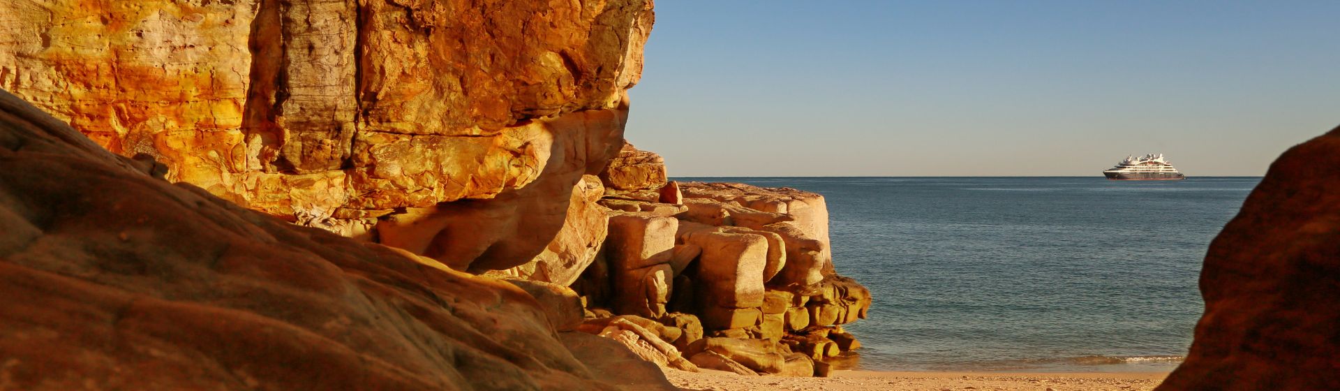 Orange rock face along the Kimberley Coastline looking out towards a cruise ship out in the ocean